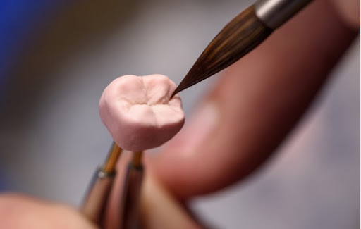 A close up of a dental technician applying a ceramic material to a dental crown