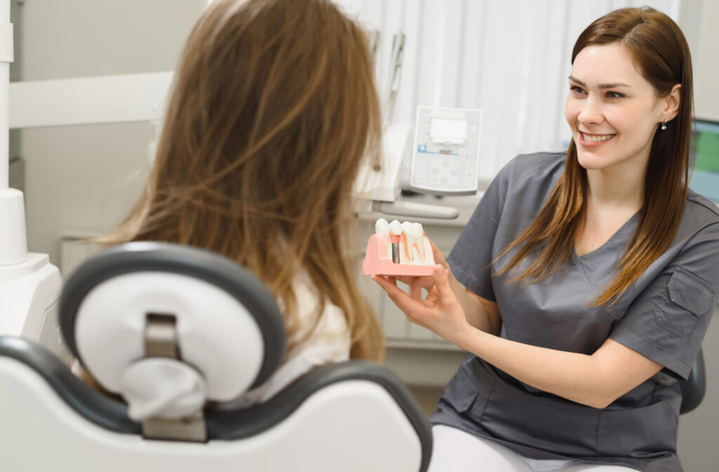 A dentist seated down beside her patient using a plastic model to help explain the process of dental implants