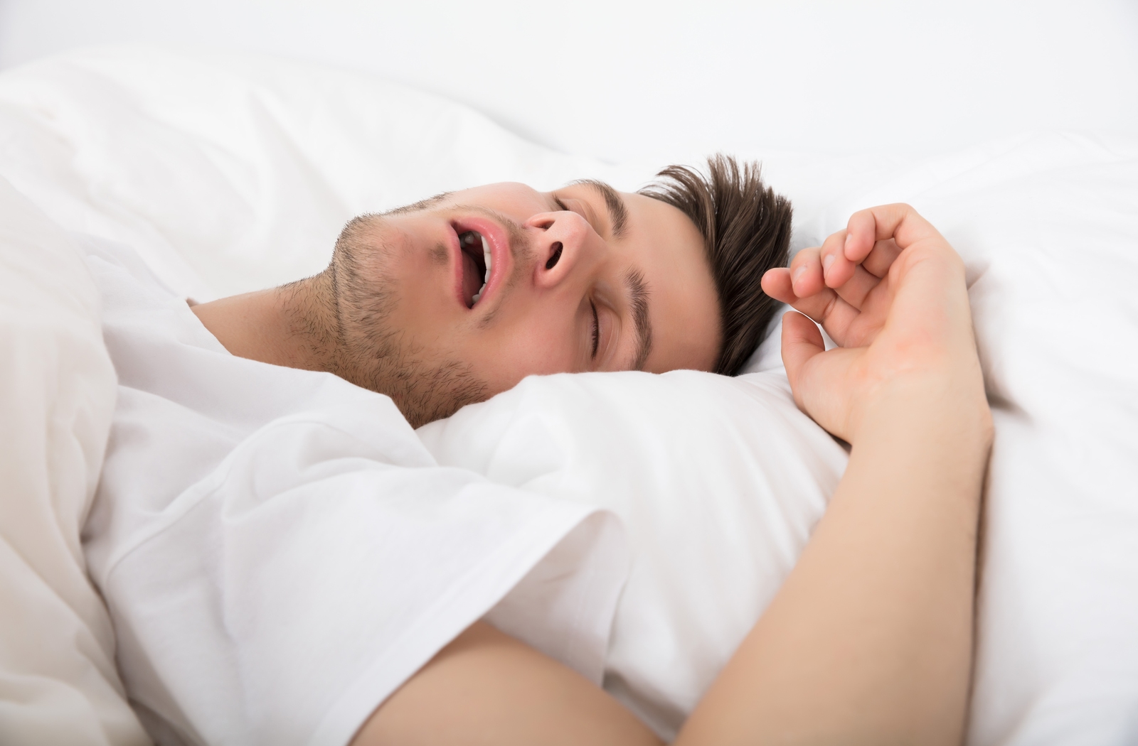 A man in bed laying under white sheets, wearing a white shirt sleeping