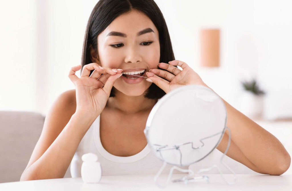 A woman looking in a mirror flossing her teeth to help prevent gum disease.