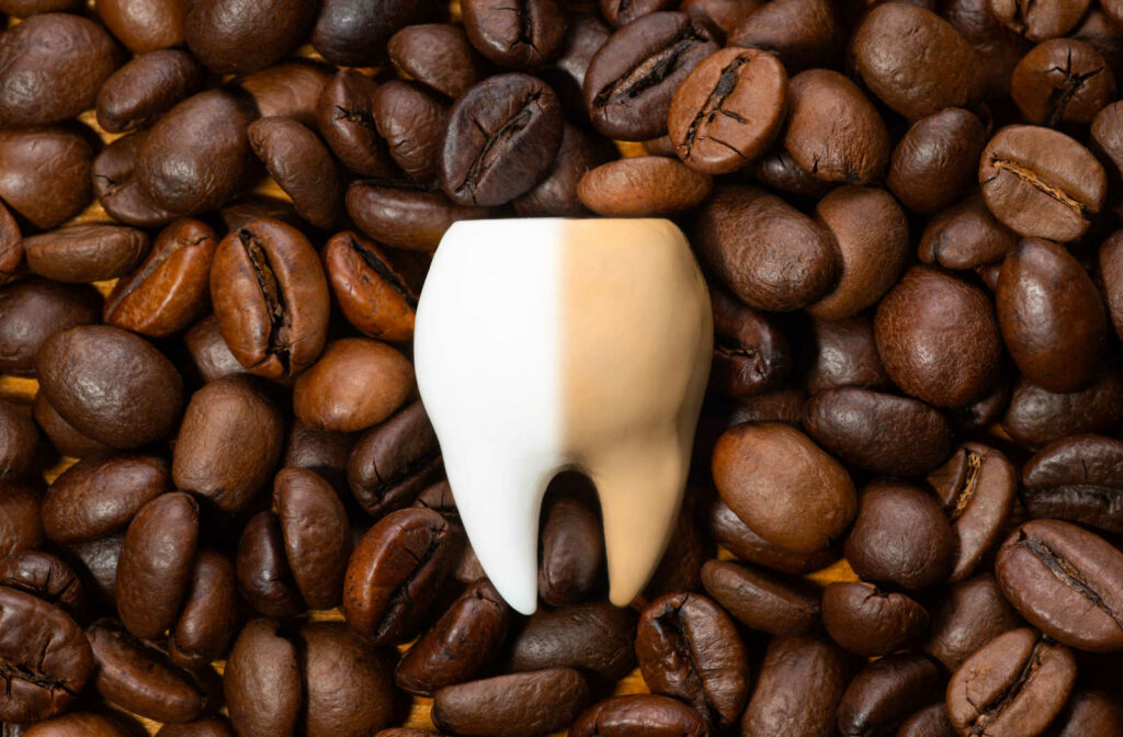 Coffee beans with a half stained tooth placed on top to show coffee can cause tooth staining.