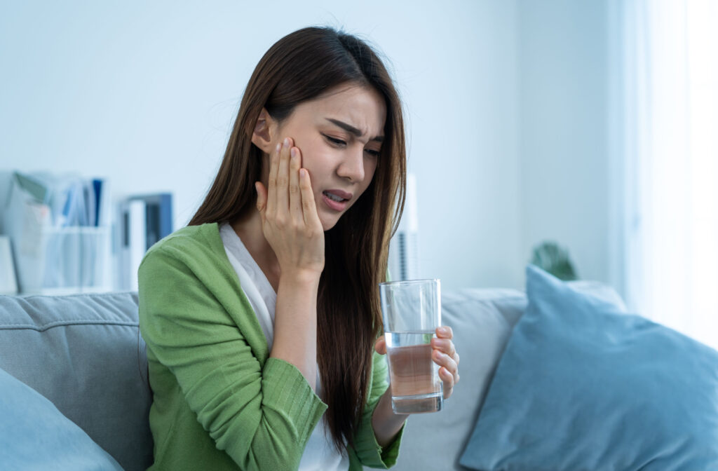 A woman holding a glass of water is in noticeable tooth pain