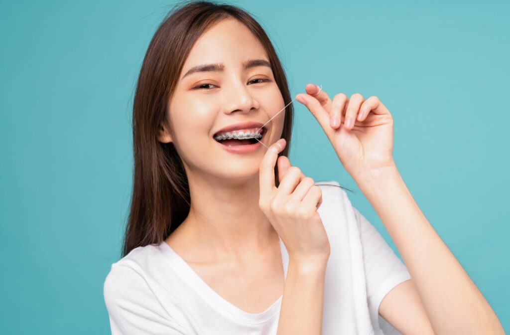 A young woman with braces using a dental floss to cleanse her teeth against a blue background