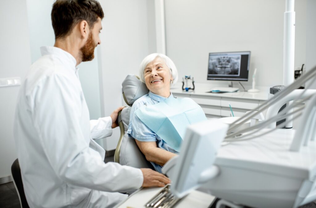 An older adult woman sitting in a dental chair and smiling at her dentist