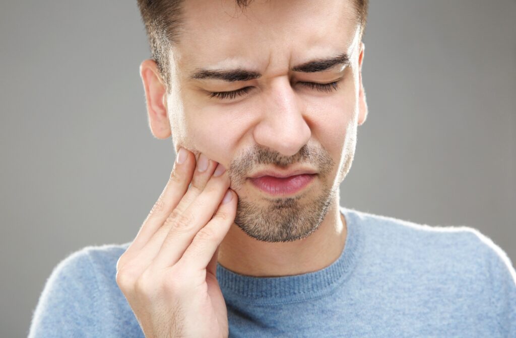 A young man squinting while rubbing his jaw due to TMJ pain.