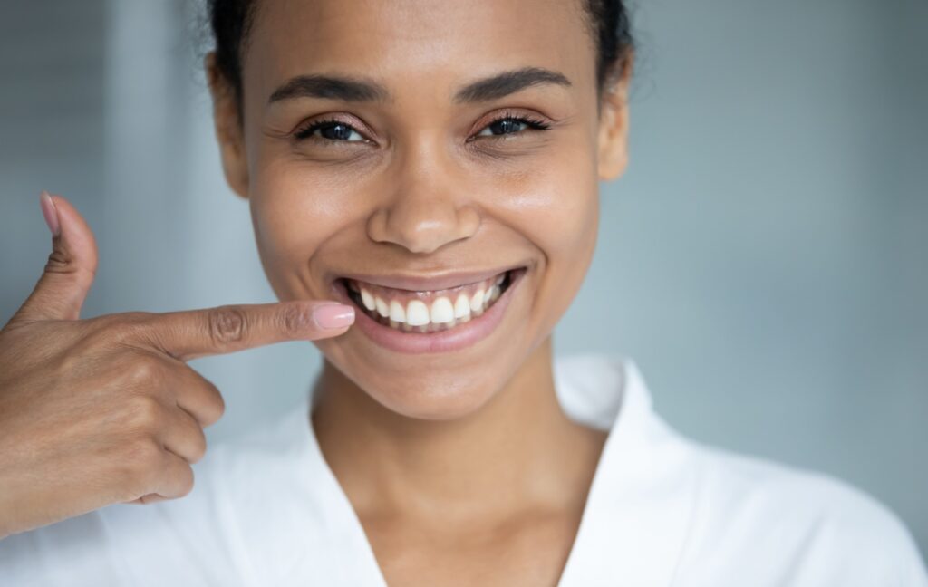 A young person wearing a white shirt smiles confidently and points towards their straight white teeth.