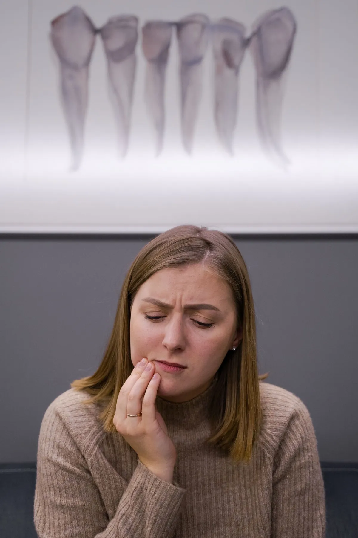 Woman holding her cheek from tooth pain before visiting an emergency dentist in Oakville